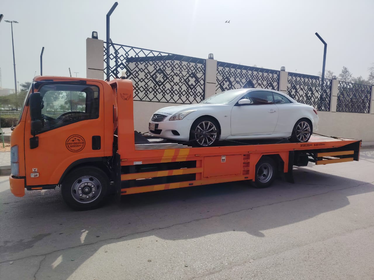 سطحة برتقالية تنقل سيارة إنفينيتي بيضاء في جدة
